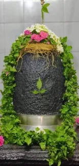 Shivling adorned with green leaves and pink flowers in a sacred setting.