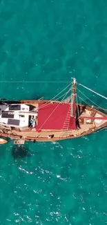 Aerial view of a sailing boat on vibrant turquoise ocean water.