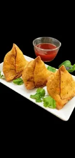 Crispy samosas and chutney on a white plate against a black background.