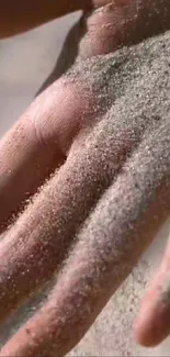 A close-up of a hand gently covered in fine sand, creating a serene texture.