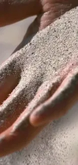 Close-up of sand flowing gently over a hand in a serene mobile wallpaper.