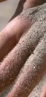 A close-up view of a hand covered with soft sand, reflecting a serene moment.