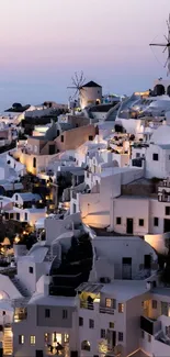 Stunning view of Santorini village at sunset with windmills and lit buildings.