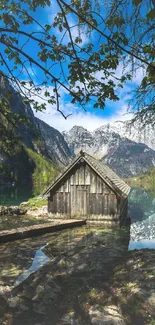Rustic cabin by alpine lake and mountains under a blue sky.