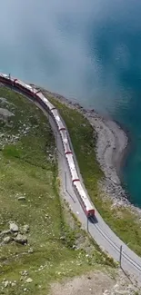 Red train on track by aqua blue lake with green hills.