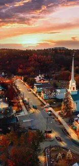 Aerial view of a town with autumn foliage and sunset sky backdrop.