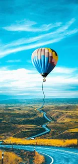 Colorful hot air balloon over scenic winding road under blue sky.