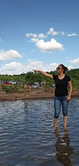 Woman standing in lake pointing with sky and clouds.