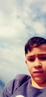 Boy takes a selfie at a cloudy beach with blue sky.