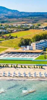 Aerial view of a beachfront resort with mountains and greenery in the background.