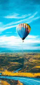 Vibrant hot air balloon in a blue sky over a vast, scenic landscape.