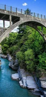 Stone bridge over turquoise river with lush green surroundings.