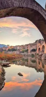 Beautiful reflection of a stone bridge over a calm river with sunset sky.