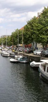 Serene canal with boats and trees on mobile wallpaper.