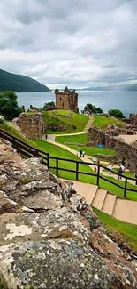 Scenic castle overlooking a lake with green hills and a cloudy sky.