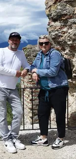 Two people pose by ancient ruins with a scenic backdrop.