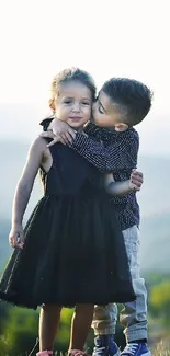 Two children embracing on a hill with a scenic nature view.