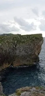 Dramatic cliff overlooking the ocean with cloudy skies in the background.