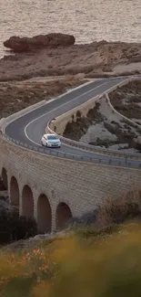 Car driving on scenic coastal road at sunset, perfect mobile wallpaper.