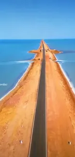 Aerial view of a scenic coastal road flanked by sea and desert under a blue sky.