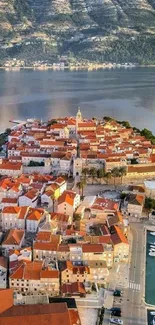 Aerial view of a coastal town with orange rooftops by the sea and mountains.