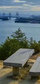 Scenic coastal bench overlooking ocean and bridge, under a blue sky.