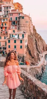 Woman walks near colorful cliffside houses at sunset.