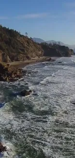 A scenic view of ocean waves crashing against a rocky shoreline under blue skies.