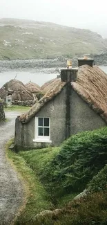 Cottage by a lake with greenery and a misty backdrop.