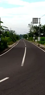 Long country road with greenery under a blue sky.