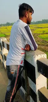 Man leaning on a bridge with scenic countryside fields.