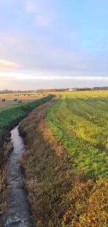 Tranquil countryside with stream and open fields under a bright sky.