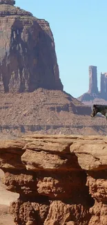 A lone rider on horseback overlooks a vast desert canyon under a clear blue sky.