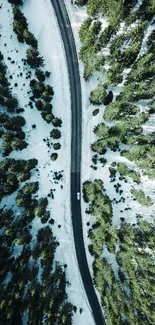 Aerial view of a forest with a road cutting through snow-touched trees.