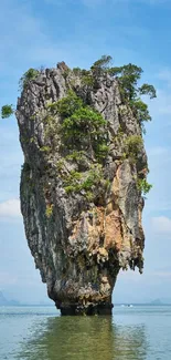 Tall island rock formation in serene blue waters under a clear sky.