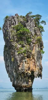 Towering island rock against blue sky and calm water.