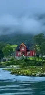 Lakefront red cottage with misty mountains and lush greenery.