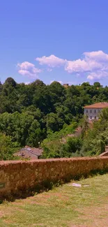 Scenic landscape with green trees, blue sky, and historic stone wall path.