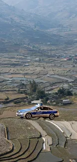 Car driving on scenic terraced fields with mountains.