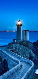 Scenic lighthouse on rocky coast at dusk with a radiant blue sky.