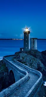 Lighthouse on rocky coast with navy blue sky.