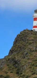 Lighthouse perched on a cliff against a vibrant blue sky.