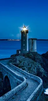 Lighthouse at night with a starry sky and tranquil ocean backdrop.