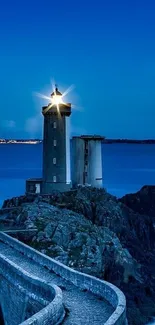 Lighthouse illuminated at night over a rocky ocean landscape.