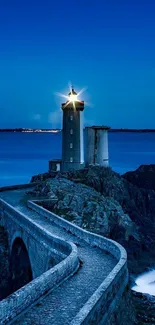 Lighthouse glowing at night on rocky cliffs with a blue ocean backdrop.