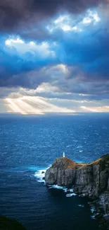 Lighthouse on cliff with ocean and beams of sunlight through clouds.