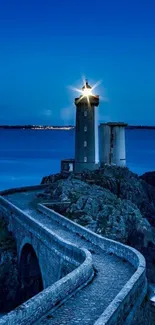 Lighthouse on rocky coast under deep blue sky at dusk.