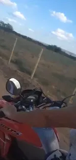 Person riding a motorcycle on a scenic country road under a blue sky.