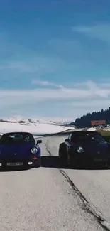 Two cars driving on a scenic mountain road under a blue sky.