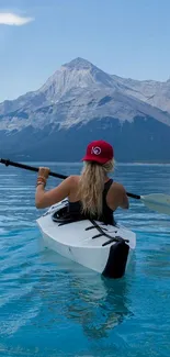 Woman kayaking on a serene blue lake surrounded by majestic mountains.